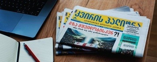 A printed issue of the “Kviris Palitra” newspaper lying on a desk next to a laptop and a notebook.